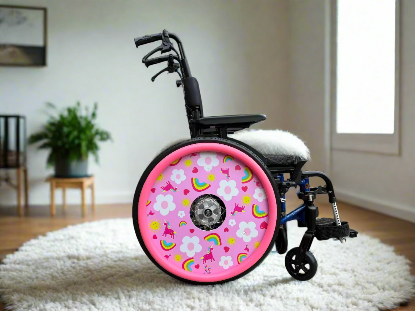 Wheelchair with a pink wheel cover featuring colorful rainbows, unicorns and flowers finished with a matching pink hand rim cover. Set on a fluffy rug.