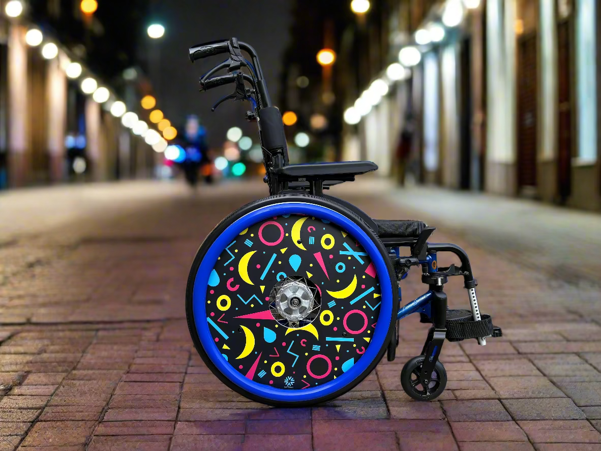 Wheelchair with rings and moons patterned wheel cover on a city street at night.
