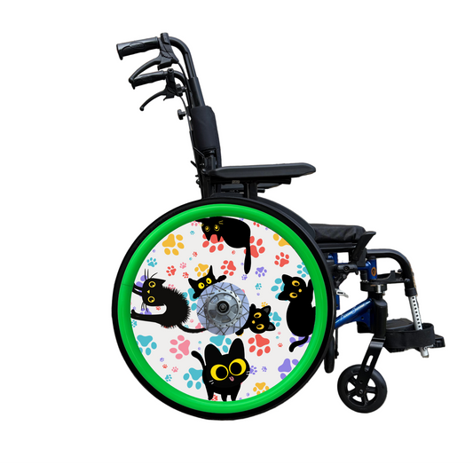 Wheelchair wheel cover on a wheelchair wit green pushrim covers. Wheel cover features black cats with orange eyes and colourful paw prints on a white background.