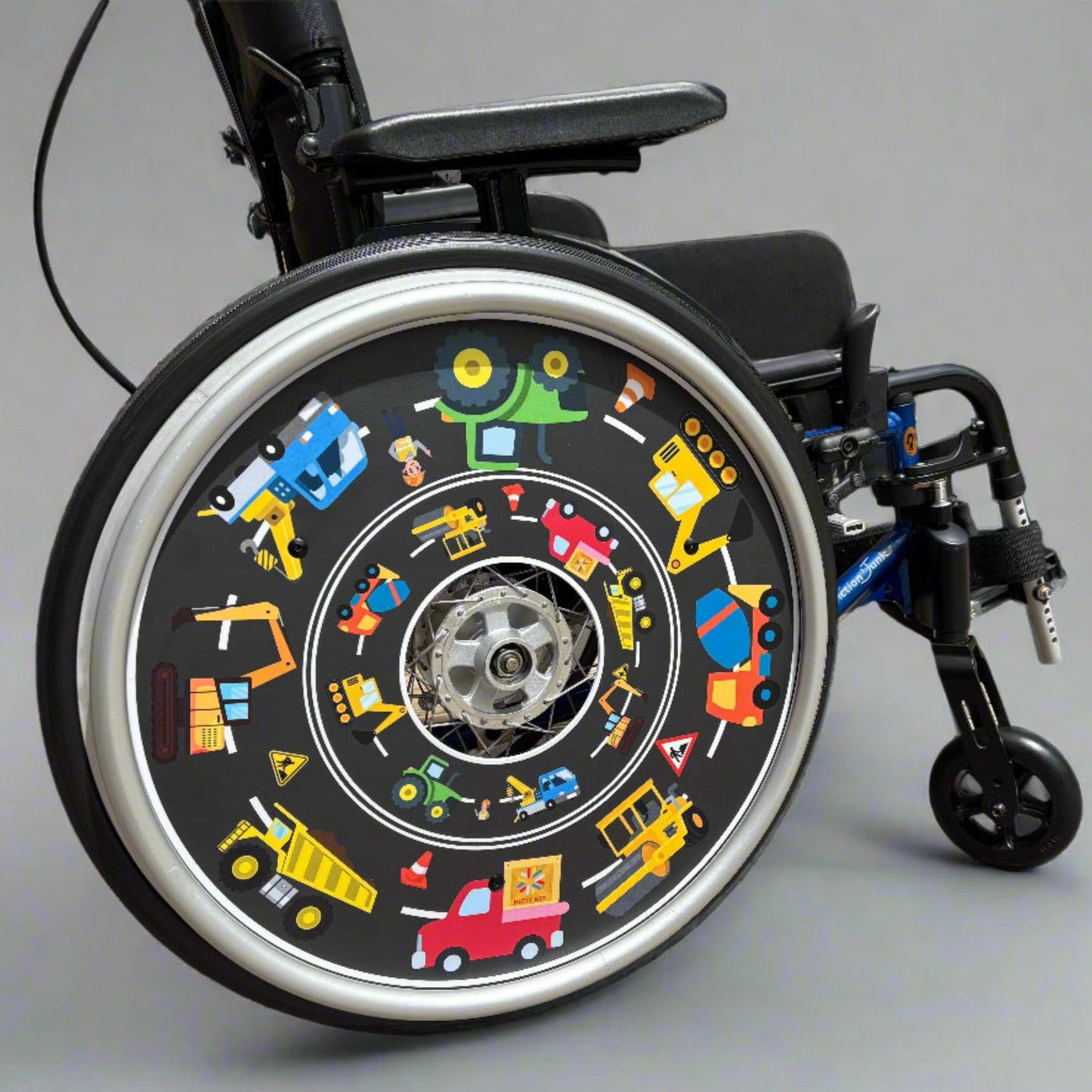 Wheelchair with a decorative wheel cover featuring colorful building site vehicle illustrations on a gray background