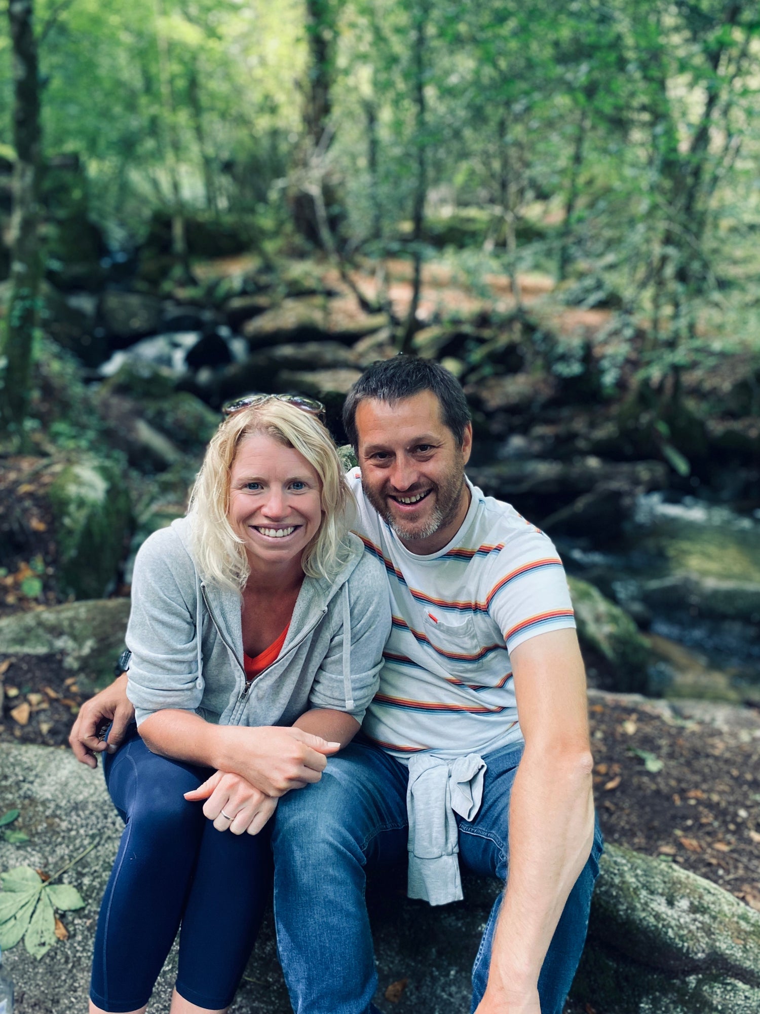 Business owners (Jess and Dan) sitting on a rock in a forest setting