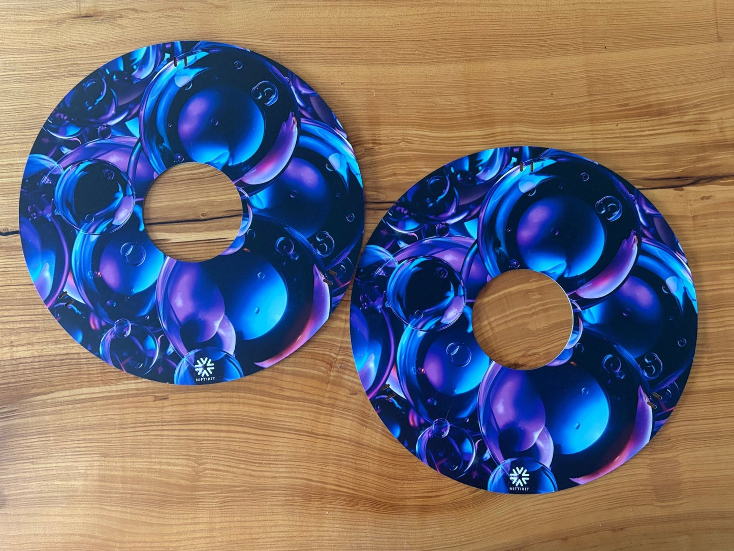 Pair of double sided wheelchair spoke guards, side 1 blue bubble design shown on a wooden surface.