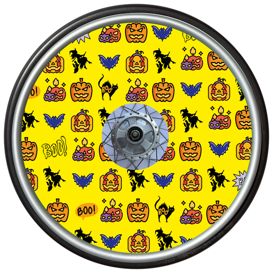 Wheelchair wheel cover on a wheel featuring pumpkins, bats, witches and Boo! on a yellow background.
