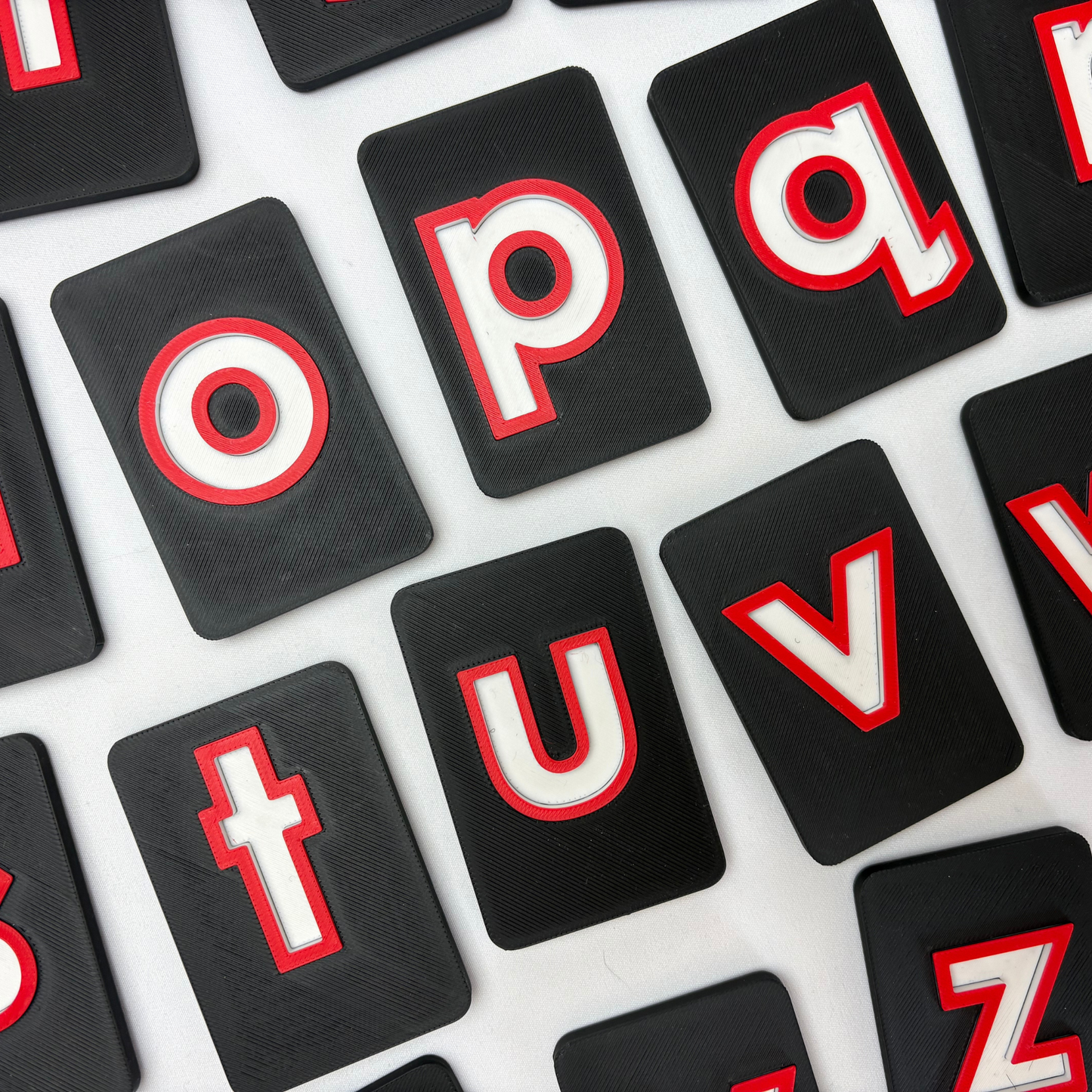 Black letter tiles with raised red and white letters . Traceable CVI friendly high contrast alphabet tiles