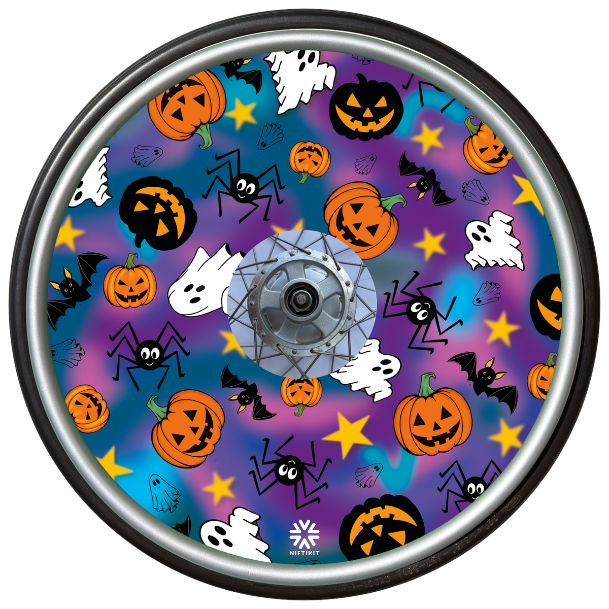 A wheelchair wheel cover or disc, featuring a colorful Halloween pattern with pumpkins, ghosts, bats, spiders, and stars on a purple and blue gradient background, surrounded by a wheel.