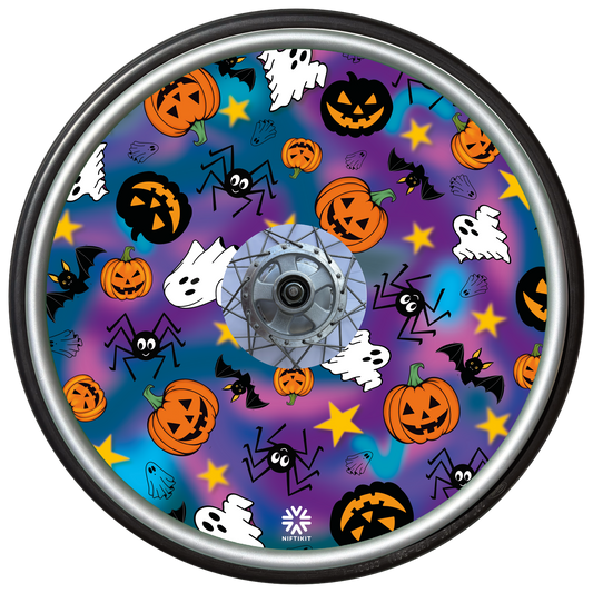 A wheelchair wheel cover or disc, featuring a colorful Halloween pattern with pumpkins, ghosts, bats, spiders, and stars on a purple and blue gradient background, surrounded by a wheel.