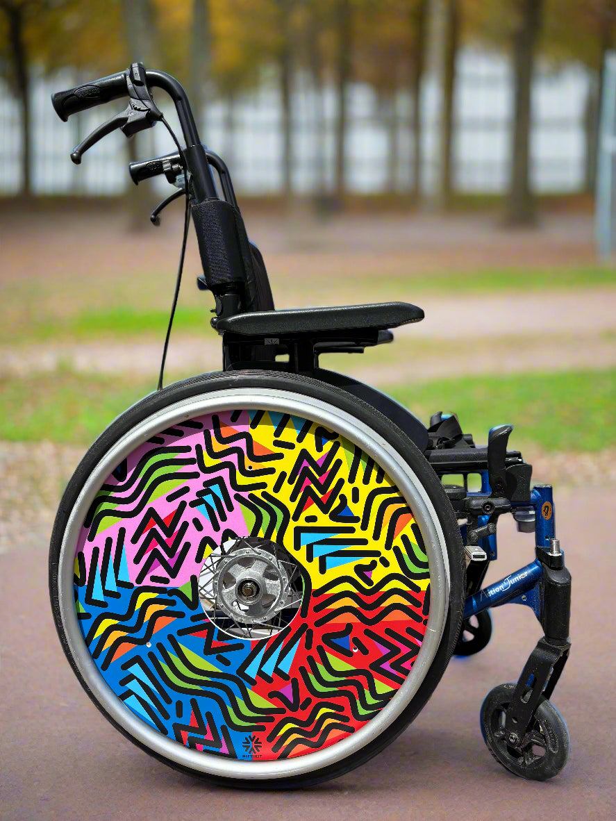 Wheelchair with wheel cover of geometric lines of varying shapes and lengths, multi-coloured background