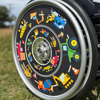 Angled wheelchair wheel featuring colourful spoke guard with tractors, diggers and trucks on a road background. 