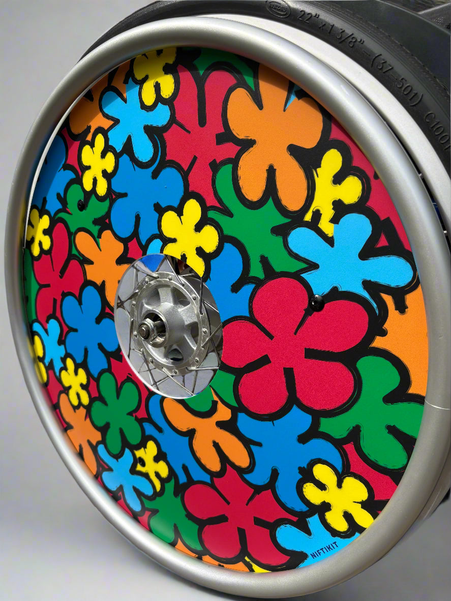 Angled wheelchair wheel with colorful, cartoon flowers spoke guard cover, in red, orange, green, yellow and blue.