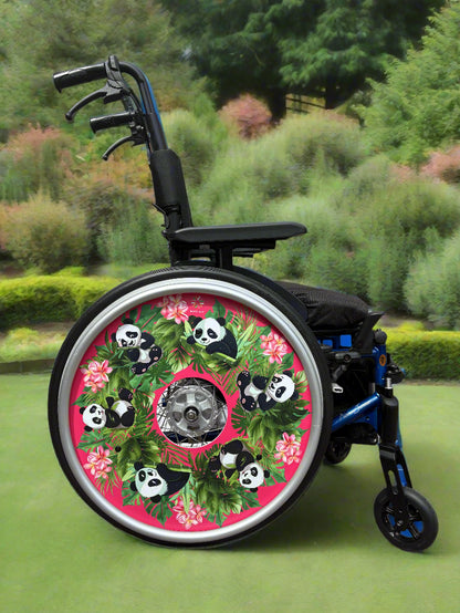 Wheelchair with wheel cover featuring cute panda illustrations, flowers, and leaves on a pink background in a garden setting. 