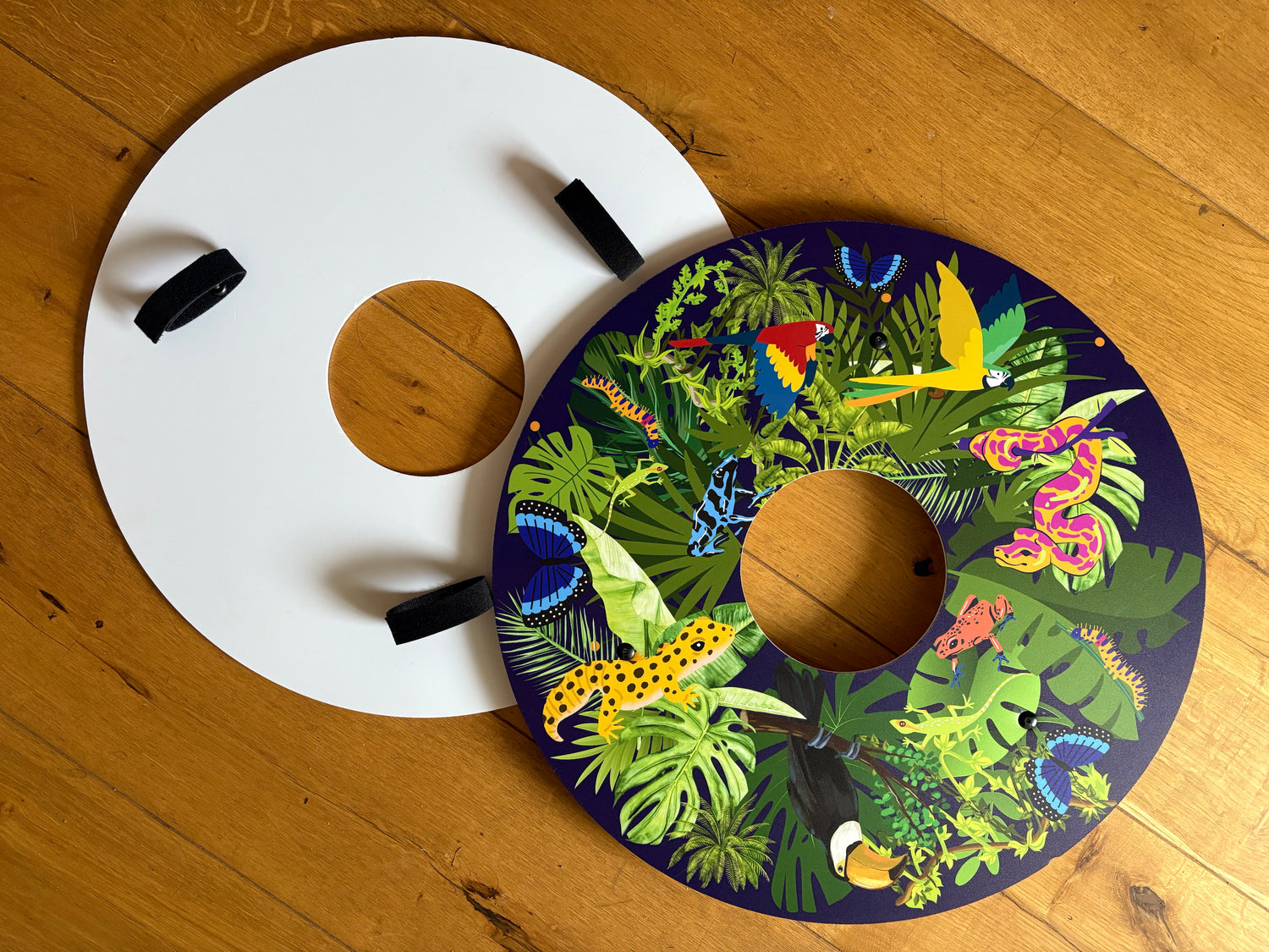 Jungle theme blue wheelchair wheel covers, spoke guards showing front and back om wooden floor background