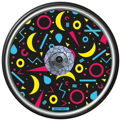 Wheelchair wheel cover with rings, lines  and moons patterns in pink, blue, yellow. Centre hub cutout, small Niftikit label. Black background. 
