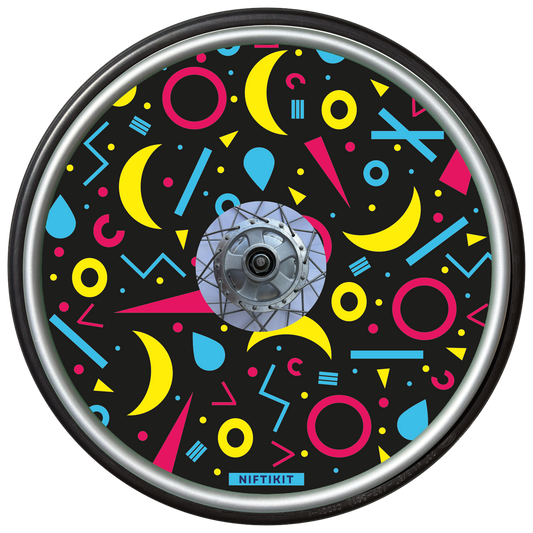 Wheelchair wheel cover with rings, lines  and moons patterns in pink, blue, yellow. Centre hub cutout, small Niftikit label. Black background. 