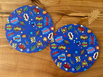 Pair of Wheelchair Spoke Guards colorful comic book style print featuring sound effects and words like 'BOOM', 'ZAP!', 'SPLASH', and 'BANG!' arranged on a wooden surface.