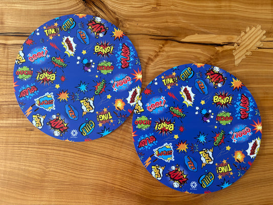 Pair of Wheelchair Spoke Guards colorful comic book style print featuring sound effects and words like 'BOOM', 'ZAP!', 'SPLASH', and 'BANG!' arranged on a wooden surface.