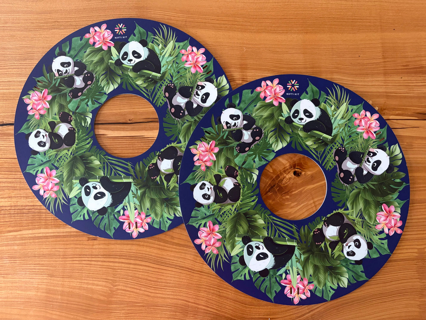 Pair of NIFTIKIT Wheelchair Spoke Guards Pandas on a navy blue background with flowers  designs on a wooden surface.