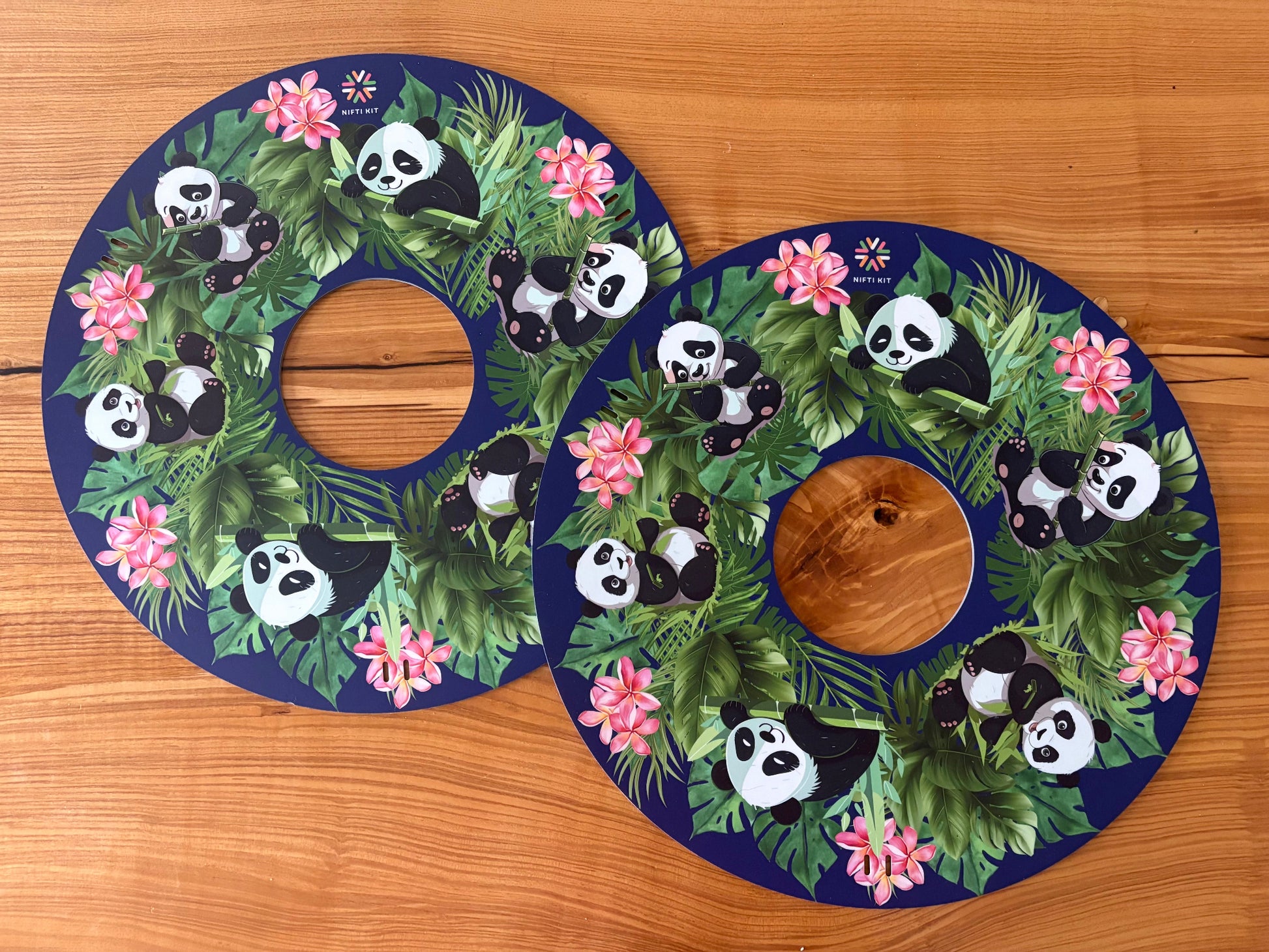 Pair of NIFTIKIT Wheelchair Spoke Guards Pandas on a navy blue background with flowers  designs on a wooden surface.