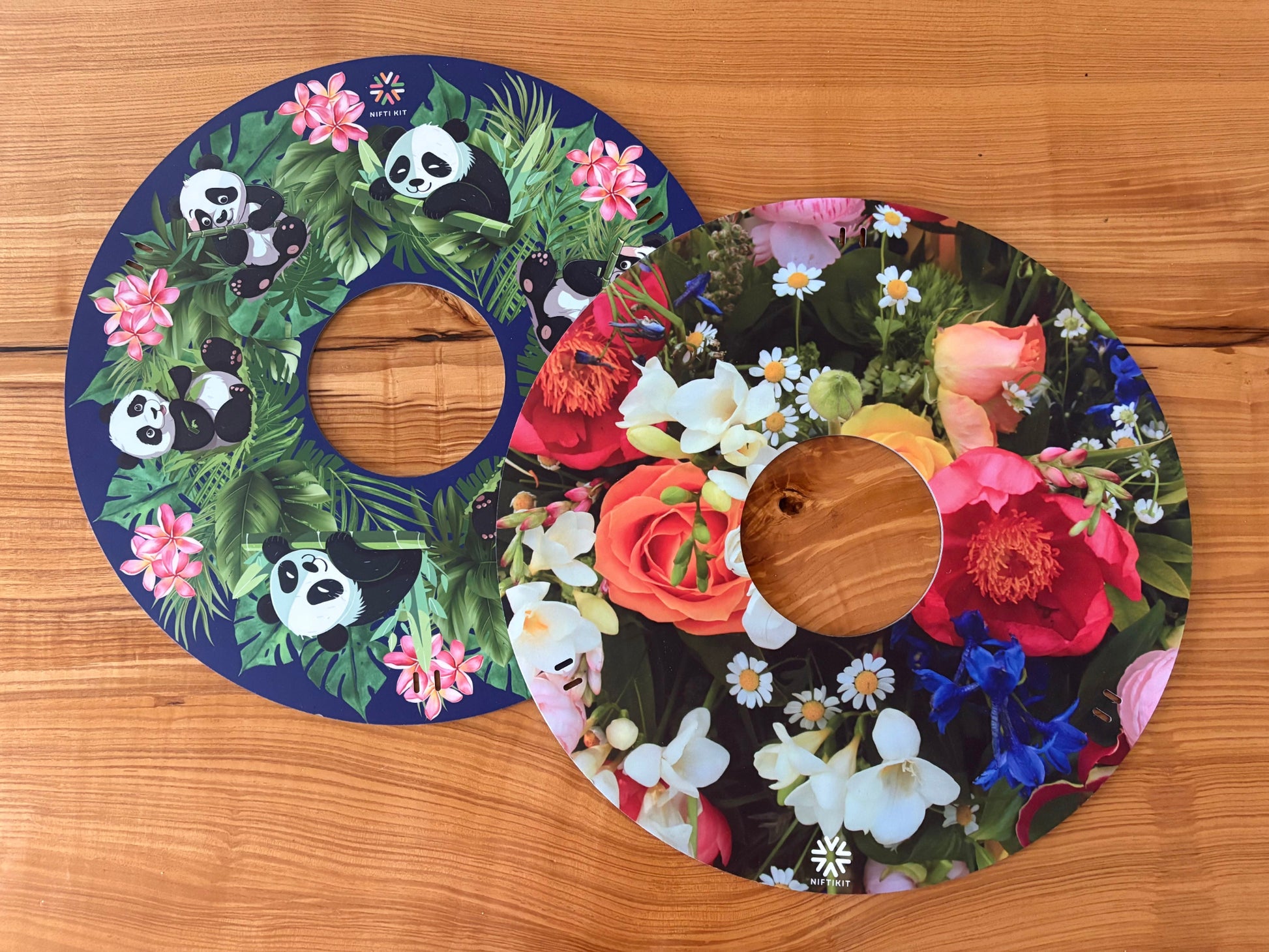 Pair of NIFTIKIT Wheelchair Spoke Guards with floral and panda designs on a wooden surface.