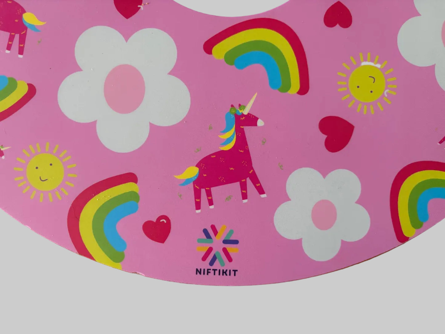 Close up of pink wheelchair wheel cover with unicorn, rainbow, and flower designs on a wooden surface. 