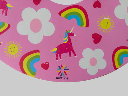 Close up of pink wheelchair wheel cover with unicorn, rainbow, and flower designs on a wooden surface. 