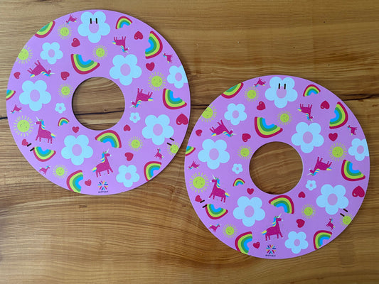 Pair of double sided wheelchair spoke guards, side Unicorns and rainbows shown on a wooden surface.