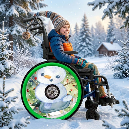 A person in a winter outfit sits in a wheelchair outdoors in a snowy forest. The wheelchair has a large decorative wheel graphic featuring a snowman in a green push rim cover.