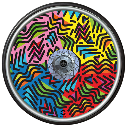 Wheelchair wheel with spoke guard featuring geometric lines of varying shapes and lengths. Background colours of 1/4 pink, 1/4 yellow 1/4 blue, 1/4 red. 