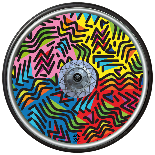 Wheelchair wheel with spoke guard featuring geometric lines of varying shapes and lengths. Background colours of 1/4 pink, 1/4 yellow 1/4 blue, 1/4 red. 