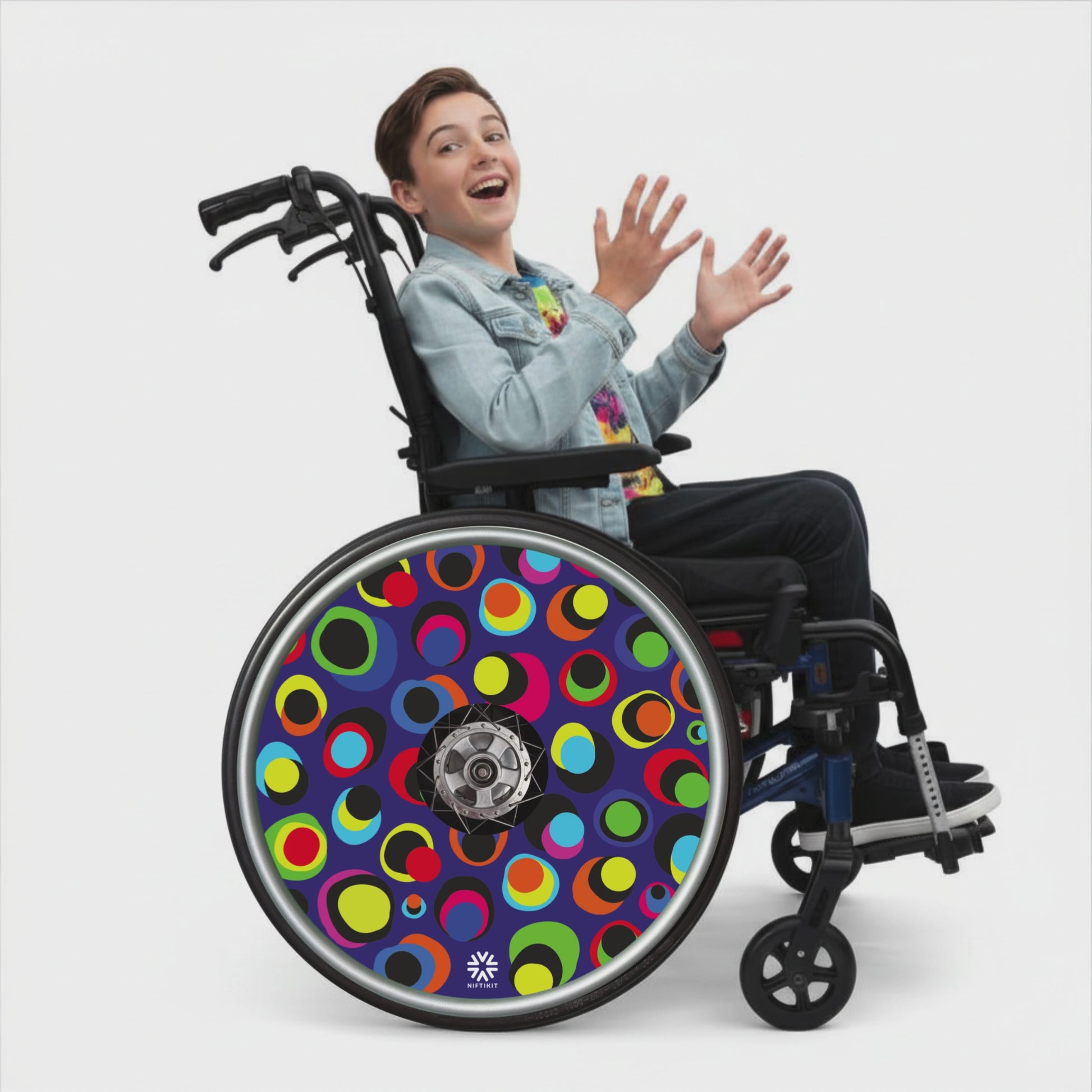 Wheelchair with rotating colourful dot pattern spoke guard covers in bright multicolour circles on a dark blue background, Niftikit Gone Dotty design